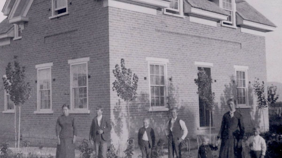 Sanie Peterson Lund standing in front of a red brick home with six children while her husband is overseas on one of his many multi-year missions that left her alone.